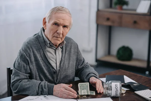 Senior man sitting at table with money, paperwork and glass jar with 'pension' lettering — Stock Photo