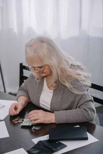 Pensionato donna in occhiali seduto a tavola e contando i soldi a casa — Foto stock