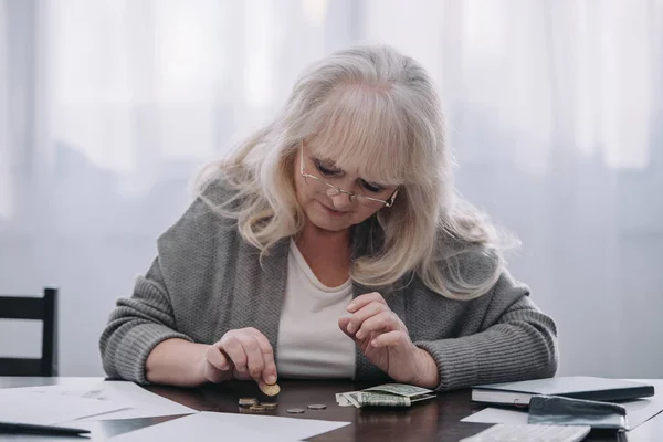 Femme retraitée assise à table et comptant l'argent à la maison — Photo de stock