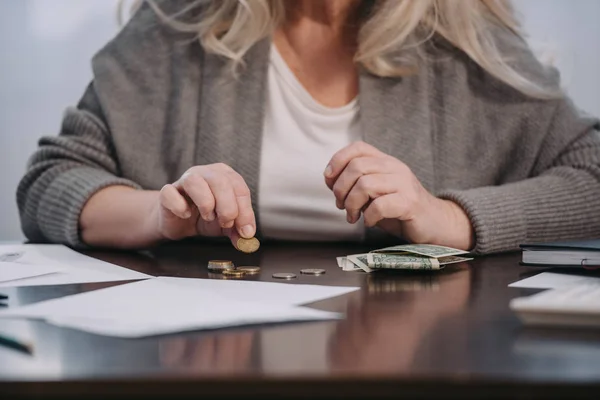 Обрезанный вид женщины-пенсионера, сидящей за столом и подсчитывающей деньги дома — стоковое фото