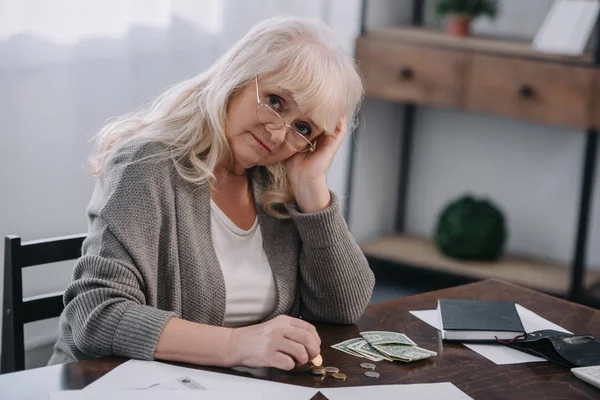 Triste retraitée assise à table, regardant la caméra et comptant l'argent à la maison — Photo de stock