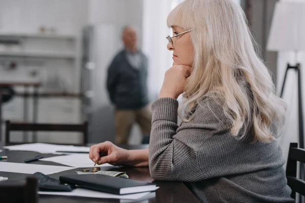 Female pensioner sitting at table and counting money at home with copy space — Stock Photo