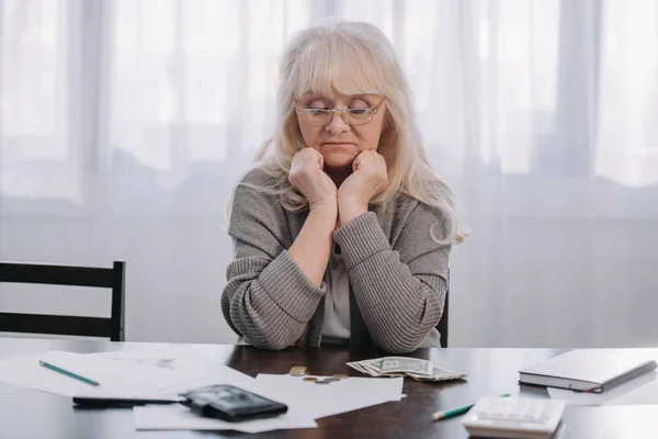 Müde Seniorin sitzt am Tisch und stützt Kopf mit Händen ab, während sie zu Hause Geld zählt — Stockfoto