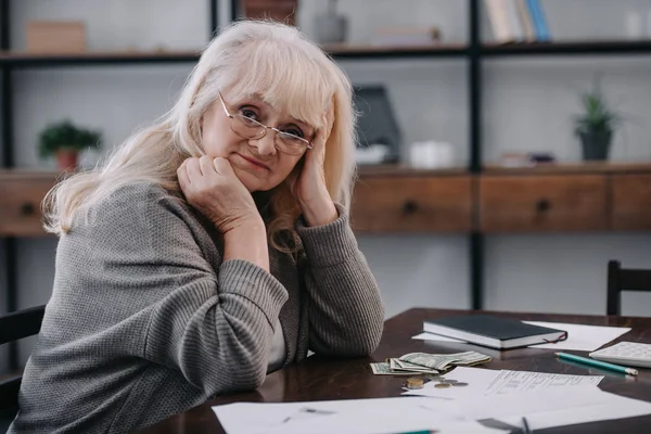 Tired senior woman sitting at table with money and paperwork while counting budget at home with copy space — Stock Photo