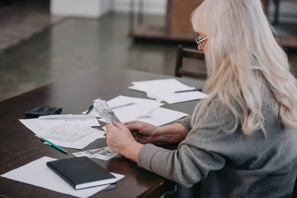 Idosa sentada à mesa com papelada e contando dinheiro — Fotografia de Stock