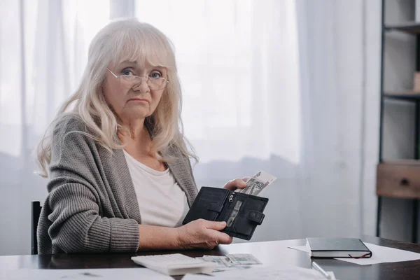 Traurige Seniorin hält Geldbörse mit Geld in der Hand und blickt in Kamera — Stockfoto