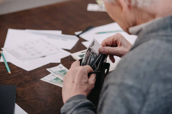 Partial view of senior man sitting at table with paperwork and counting money — Stock Photo