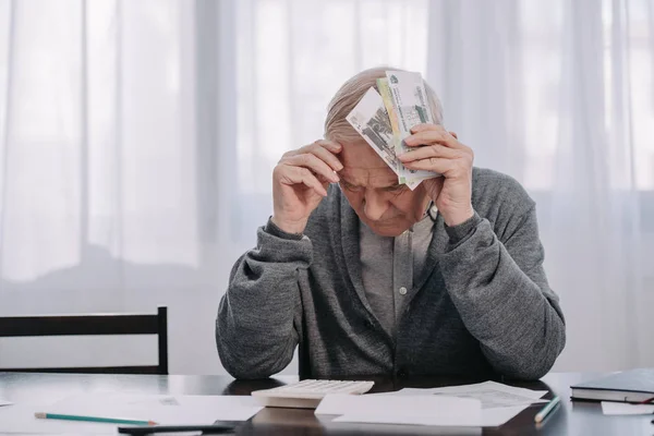 Стресс старший человек сидит за столом с бумажной работой и проведение денег на дому — стоковое фото