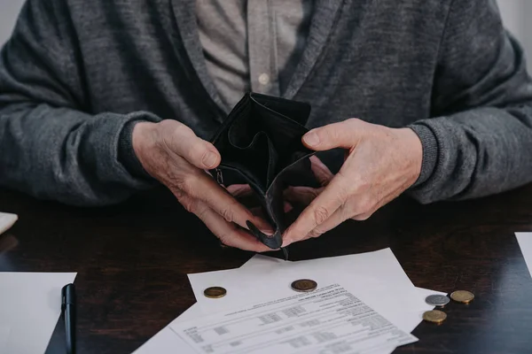 Vista recortada del pensionista masculino sentado a la mesa con papeleo y con la cartera vacía - foto de stock