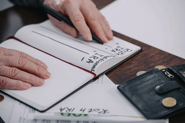 Vista recortada de la mujer mayor sosteniendo pluma cerca del cuaderno con roth ira e ira tradicional palabras - foto de stock