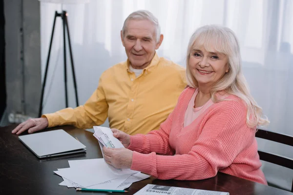 Feliz pareja de ancianos sosteniendo sobre con dinero y mirando a la cámara - foto de stock