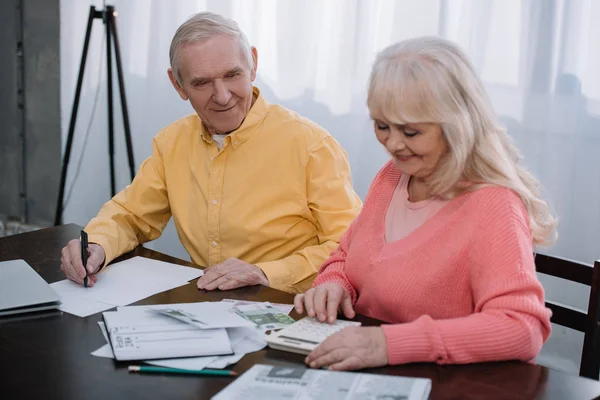 Senior coupe sitting at table with calculator and counting money — стоковое фото