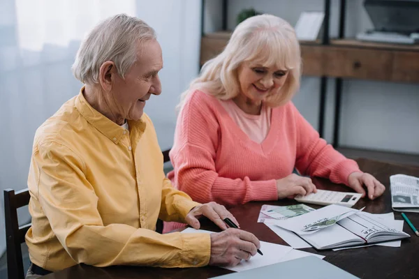 Sonriendo cupé senior sentado en la mesa con calculadora y contando dinero - foto de stock