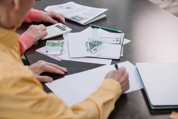 Старша пара сидить за столом з паперовою роботою, конверт з написом і грошима — стокове фото