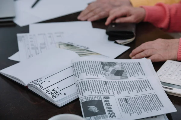 Cropped view of senior couple sitting at table with business newspaper, envelope with 'roth ira' lettering and notebook — Stock Photo