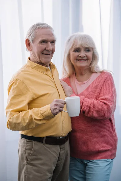 Sorrindo casal sênior em roupas casuais com xícara de café em casa — Fotografia de Stock