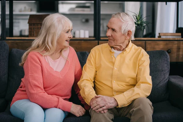 Пожилая пара в повседневной одежде сидит на диване и смотрит друг на друга в гостиной — стоковое фото