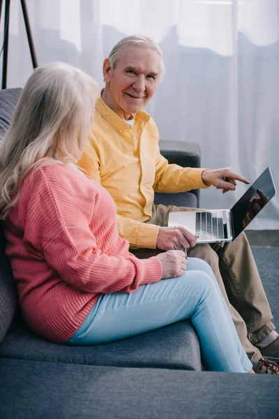 Casal sênior sentado no sofá e usando laptop em casa — Fotografia de Stock