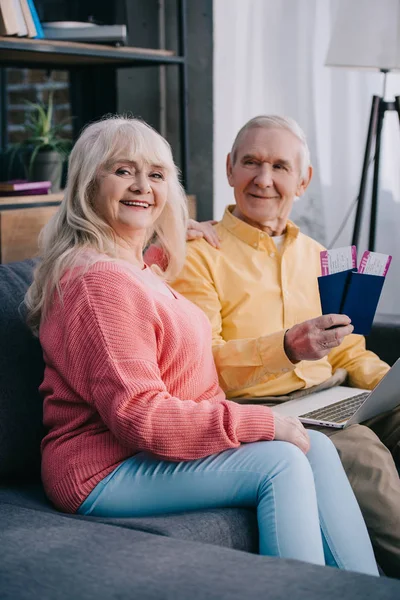 Smiling senior couple sitting on couch with air tickets and passports at home — Stock Photo
