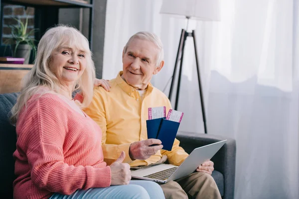Älterer Mann hält Flugtickets und Pässe in der Hand, während ältere Frau Daumen hoch zeigt und in die Kamera blickt — Stockfoto
