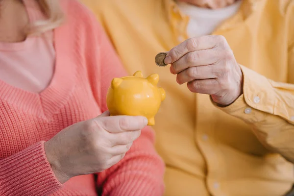 Cropped view of senior couple putting coin in yellow piggy bank — Stock Photo