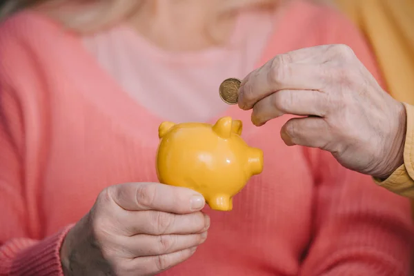 Vue recadrée de l'homme âgé mettant pièce en tirelire jaune — Stock Photo