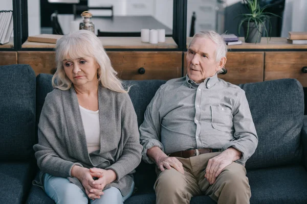 Грустная одинокая старшая пара в повседневной одежде сидит дома на диване — стоковое фото