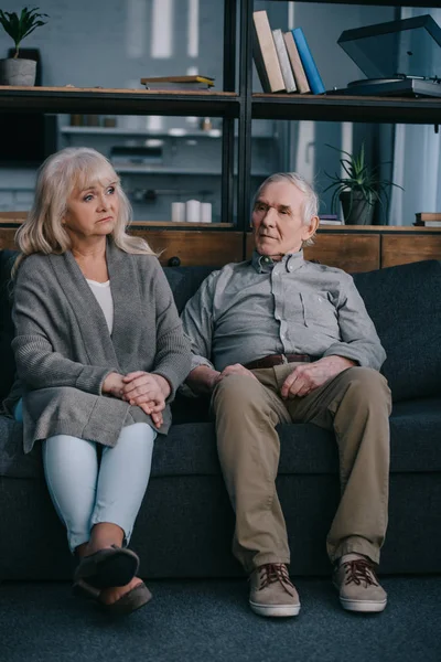 Triste couple âgé solitaire en vêtements décontractés assis sur le canapé à la maison — Photo de stock