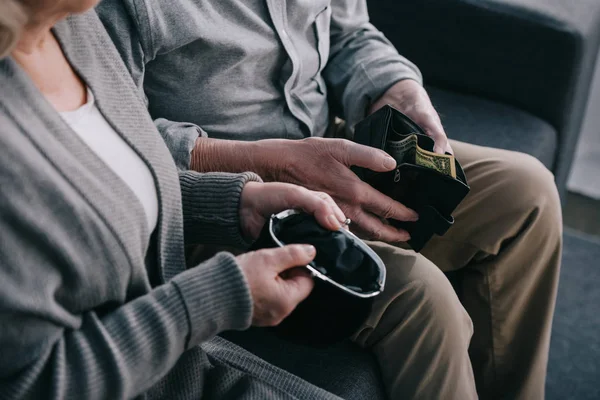 Cropped view of senior couple sitting on couch and holding wallets at home — Stock Photo