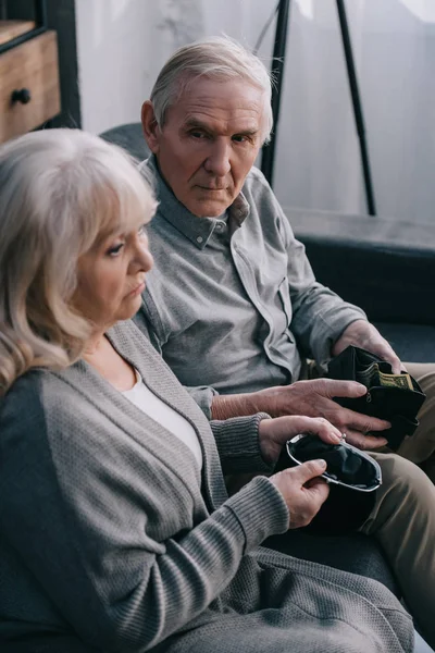 Triste couple âgé assis sur le canapé et tenant des portefeuilles à la maison — Photo de stock