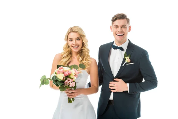 Улыбающаяся невеста с красивым свадебным букетом, и жених в элегантном черном костюме изолированы на белом — стоковое фото