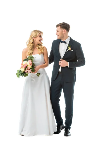 Hübsche Braut im Hochzeitskleid und schöner Bräutigam im eleganten schwarzen Anzug, die sich isoliert auf Weiß betrachten — Stockfoto