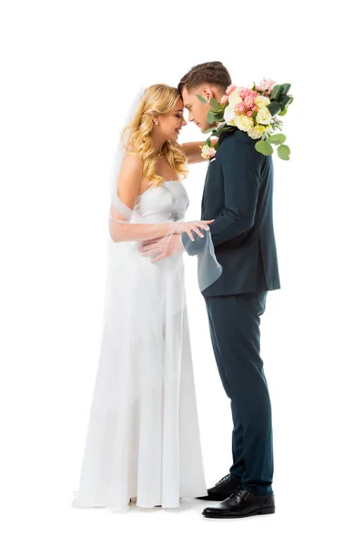 Pretty bride in white wedding dress, and groom in elegant black suit standing face to face isolated on white — Stock Photo