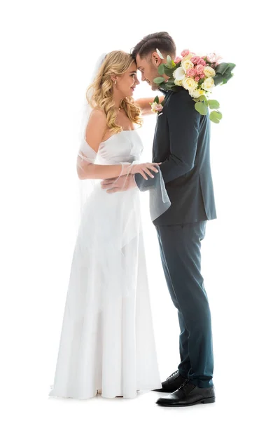 Beautiful bride in white wedding dress, and groom in elegant black suit standing face to face isolated on white — Stock Photo