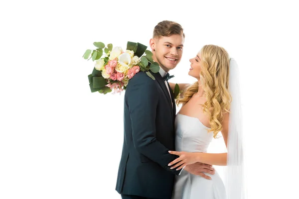 Glückliche Braut mit Brautstrauß umarmt lächelnden Bräutigam isoliert auf weiß — Stockfoto