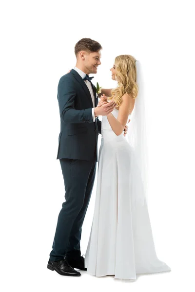 Happy bride in white wedding dress dancing with smiling groom in black elegant suit isolated on white — Stock Photo