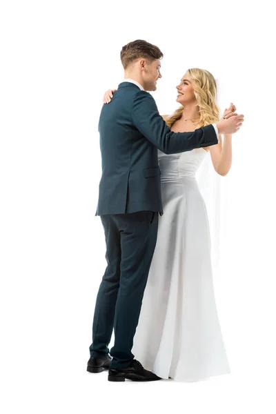 Novio sonriente en traje elegante negro bailando con novia feliz en vestido de novia blanco aislado en blanco - foto de stock