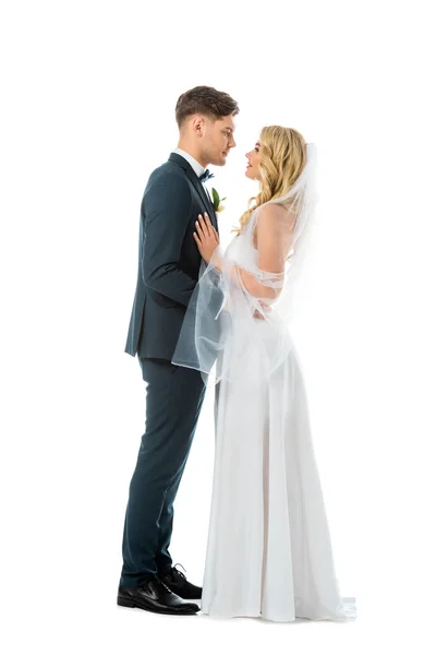 Beautiful bride in long wedding dress and handsome groom in elegant suit standing face to face isolated on white — Stock Photo