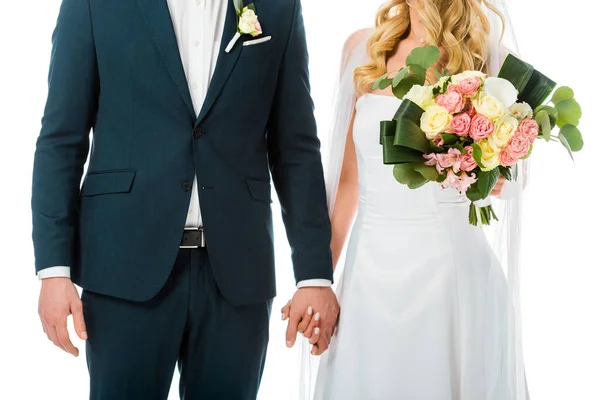 Vista cortada da noiva com belo buquê de casamento de mãos dadas com o noivo em terno elegante isolado no branco — Stock Photo