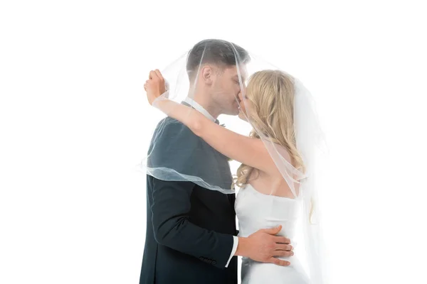 Noiva feliz beijando noivo enquanto o cobre com véu nupcial isolado no branco — Fotografia de Stock
