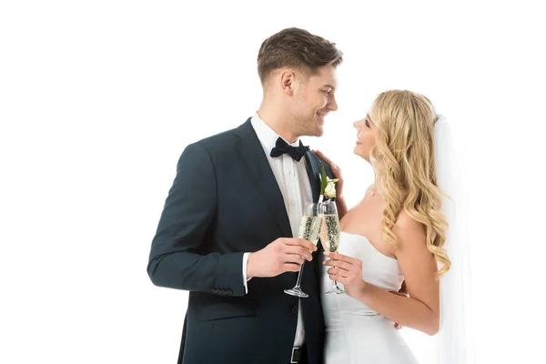 Happy bride and groom clinking glasses of champagne and looking at each other isolated on white — Stock Photo