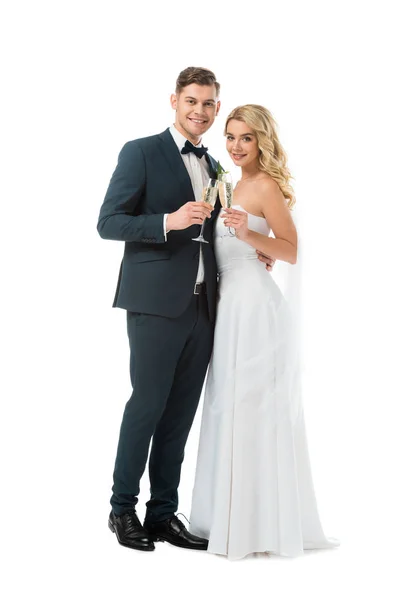 Happy bride and groom holding glasses of champagne and looking at camera isolated on white — Stock Photo