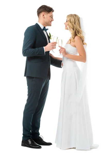 Alegre novia y novio tintineo copas de champán y mirándose aislados en blanco - foto de stock