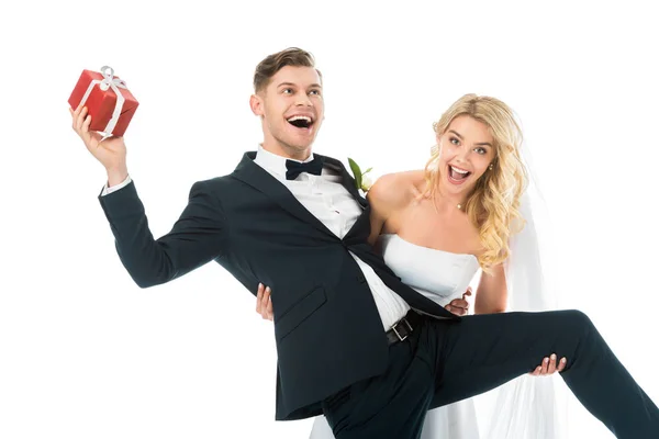 Fröhliche Braut und lächelnder Bräutigam mit Geschenkbox, die Spaß haben isoliert auf Weiß — Stockfoto