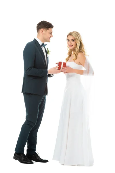 Beau marié souriant présentant boîte cadeau à belle mariée isolé sur blanc — Photo de stock