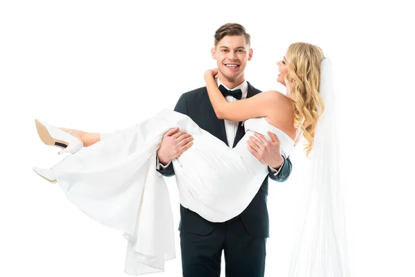 Sonriente guapo novio celebración feliz hermosa novia en manos aisladas en blanco - foto de stock