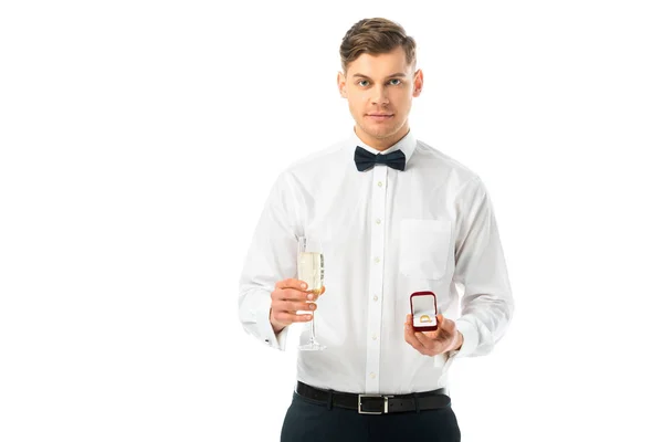 Bonito noivo segurando copo de champanhe e caixa de presente com anel de casamento isolado no branco — Fotografia de Stock