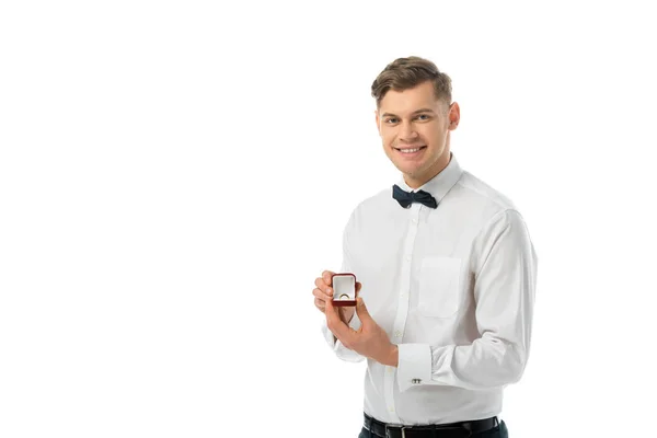 Sonriente novio sosteniendo caja de regalo con anillo de boda y mirando a la cámara aislada en blanco - foto de stock