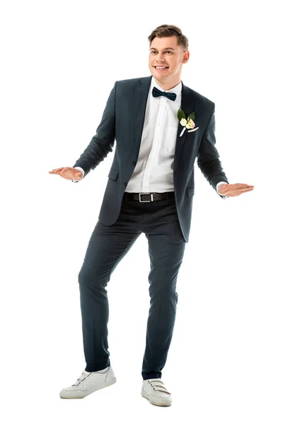 Feliz novio joven bailando en traje elegante negro y zapatillas blancas aisladas en blanco - foto de stock