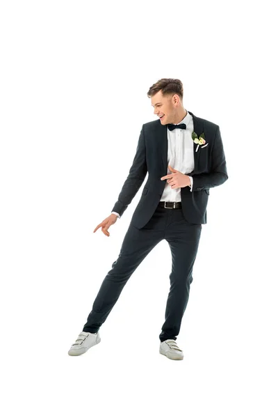 Alegre novio bailando en traje negro y zapatillas blancas aisladas en blanco - foto de stock